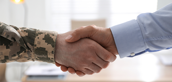 Close up photo of a handshake with the hand on the left is from someone in uniform and the one on the right is of someone in a dress shirt. 