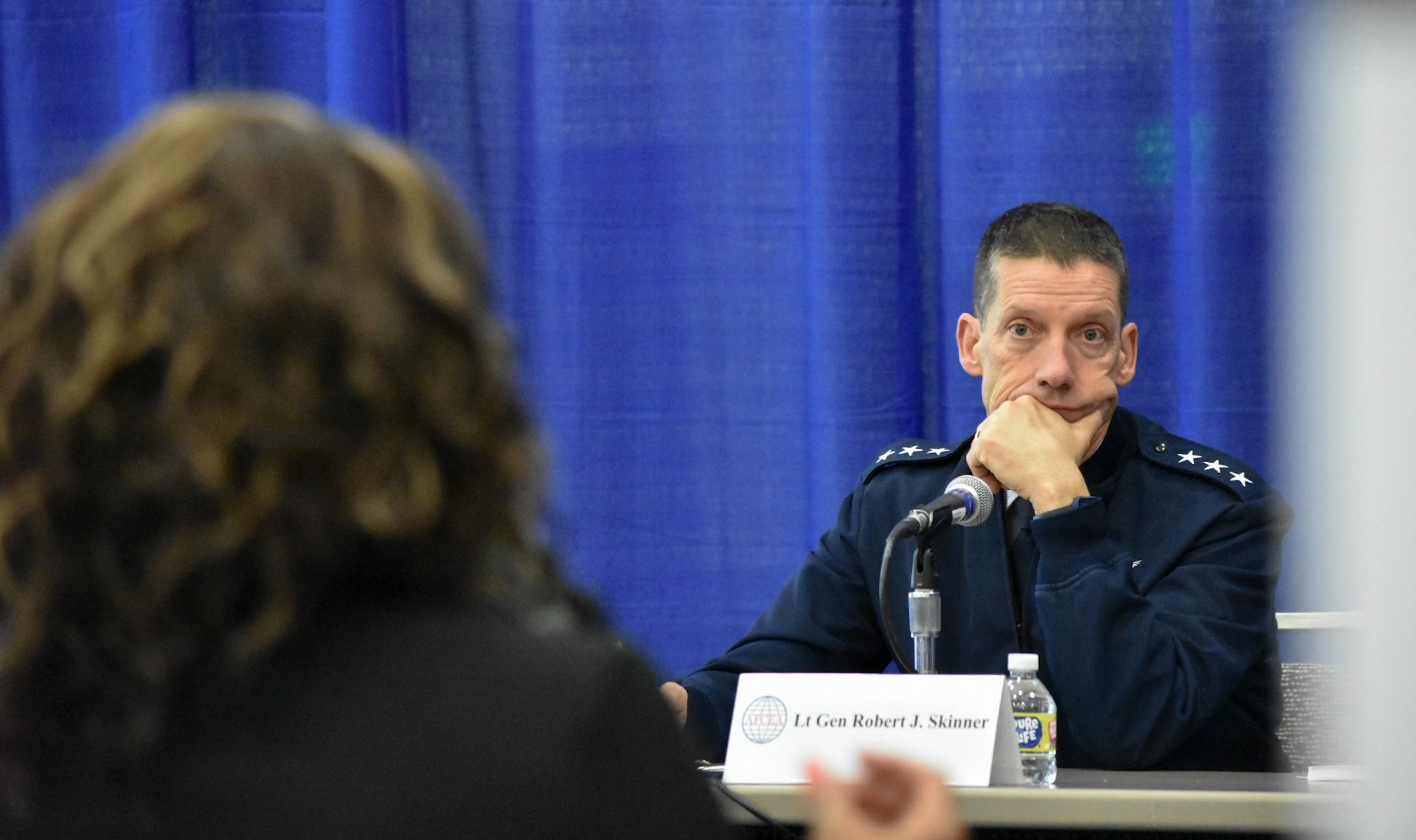 Photo of Lt. Gen. Skinner sitting at the panel table leaning his chin on his hand, focused on a competitor .
