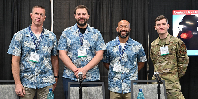 Photo of (from left) Brad Wright, Steve Mathews, Brandon Glover and Air Force Capt. Timothy Kokotajlo posing for the picture while standing behind a table at their theater session, "DISA Hybrid Cloud Broker: Recognizing Mission Requirements to Deliver Solutions."