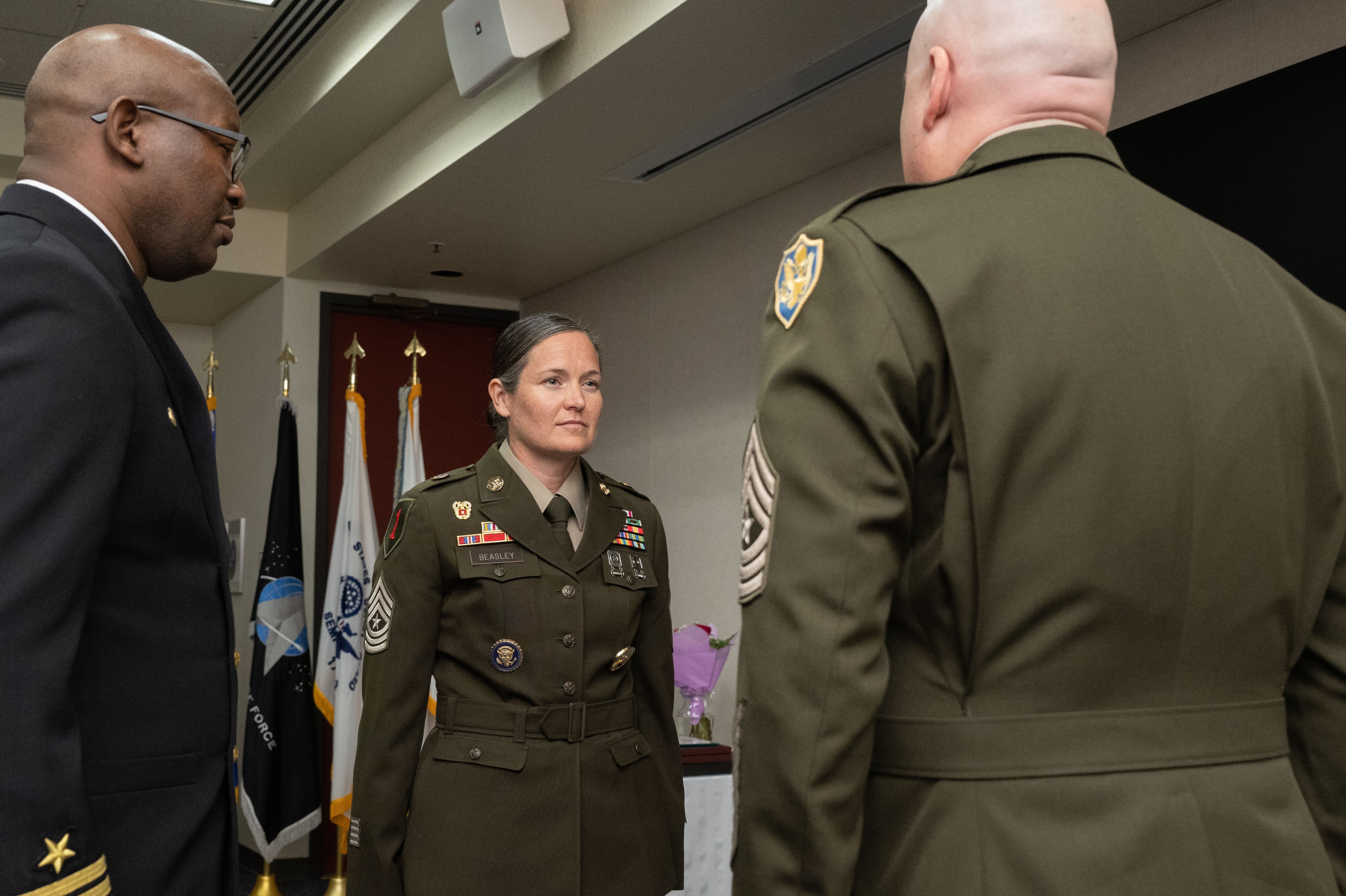 JITC Commander Navy Capt. Anthony T. Saxon is on the left looking right while Army Sgt. Maj. Ashley M. Beasley is in the center of the image facing slightly to the right at Army Sgt. Maj. James R. Whitcomb who is on the right side of the image with his back to the camera.